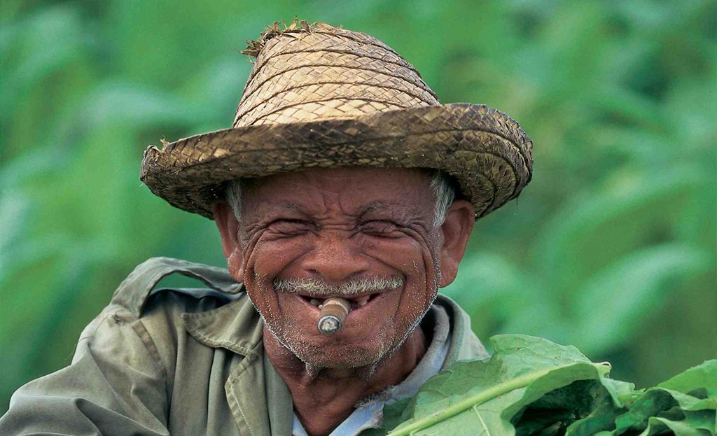 Portrait souriant d'un paysan cubain en chapeau de paille fumant un cigare, région de Piñar del Río
