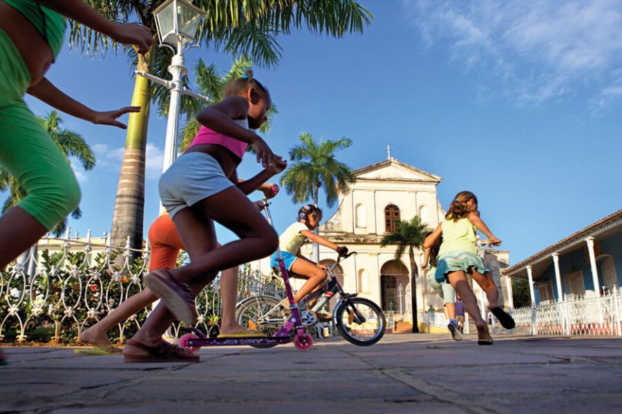 Enfants jouant à vélo et trottinette devant une église coloniale à Trinidad, Cuba