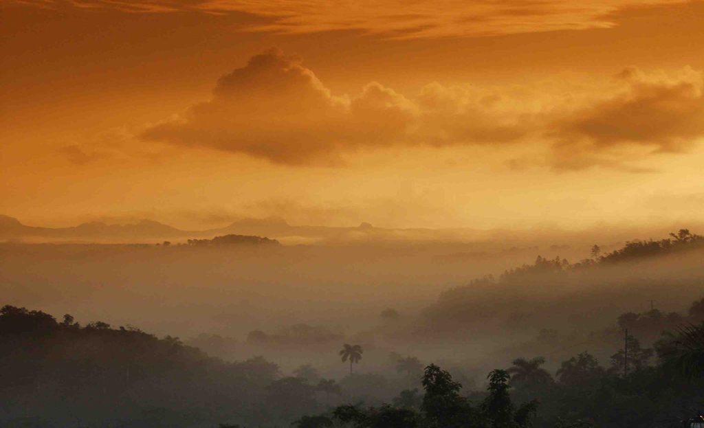Ciel orangé et brume matinale sur les collines boisées de Viñales, Cuba