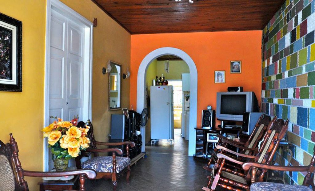 Intérieur coloré d'une maison cubaine avec fauteuils à bascule, télévision et arche vers cuisine, Viñales