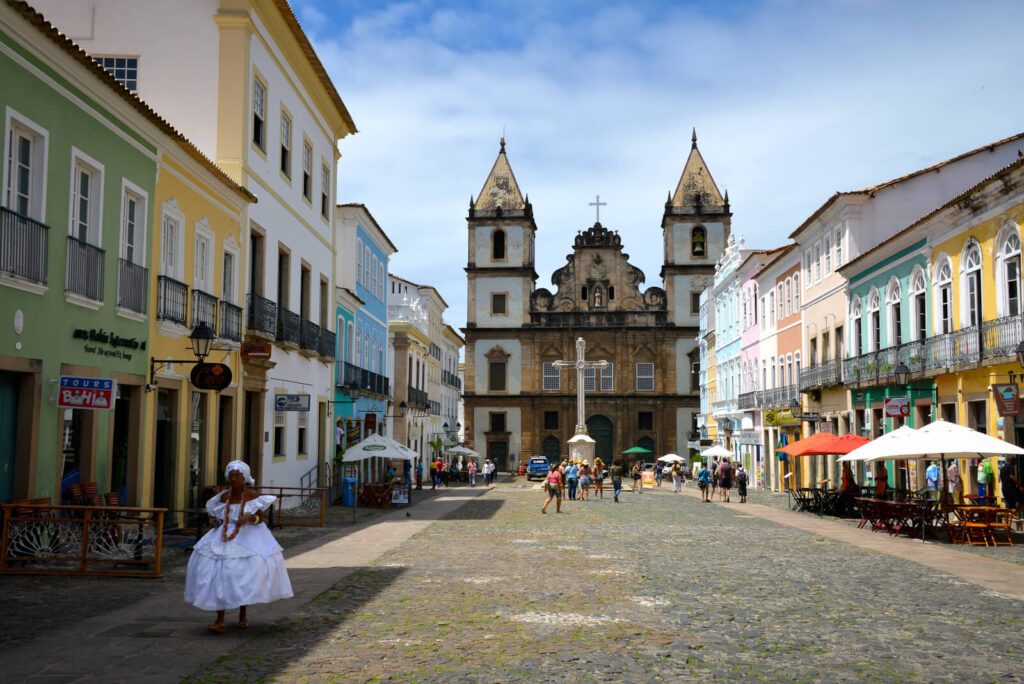 Place pavée du Pelourinho avec église baroque, façades colorées et femme en tenue traditionnelle blanche, Salvador de Bahia