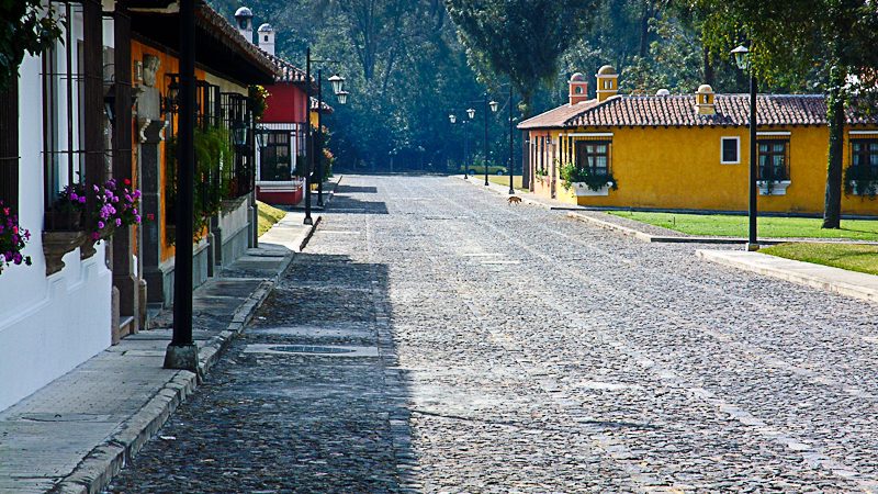Rue pavée à Antigua avec façades coloniales colorées et fleurs violettes en pot, Guatemala