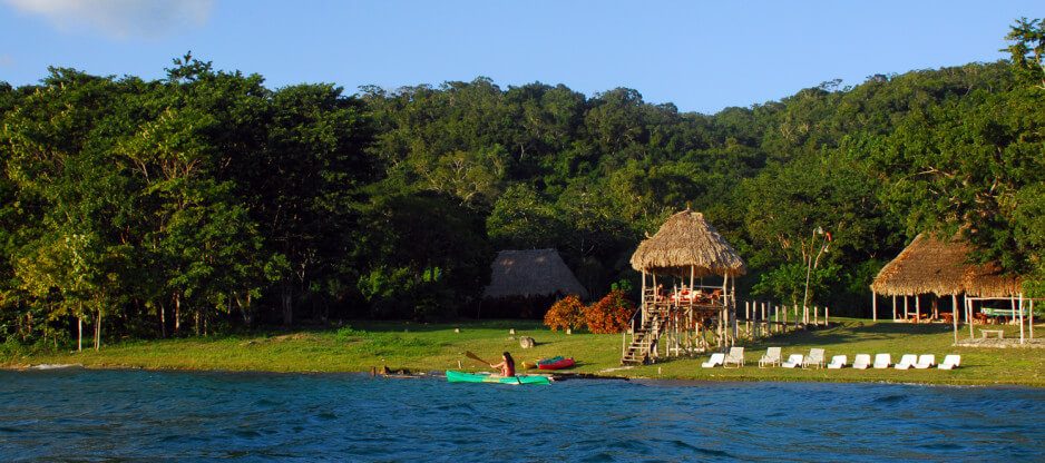 Rive boisée avec kayak sur l'eau et huttes en chaume au Guatemala