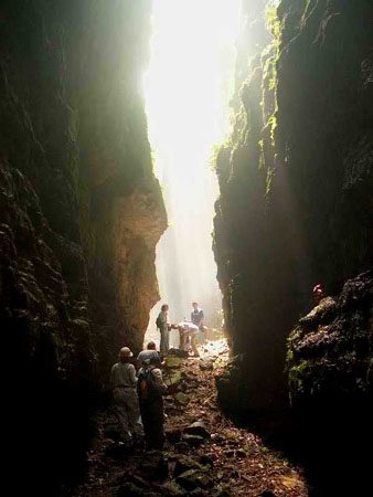 Randonneurs traversant une faille rocheuse étroite éclairée par la lumière, Aguateca, Guatemala