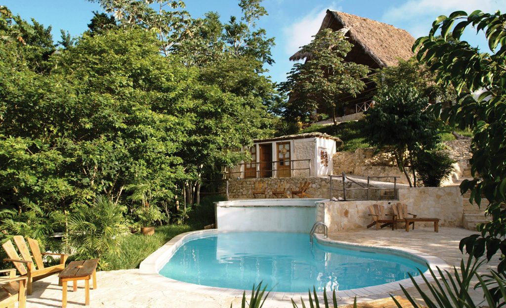 Piscine et lodge en pierre avec toit de chaume entourés de forêt tropicale, Guatemala