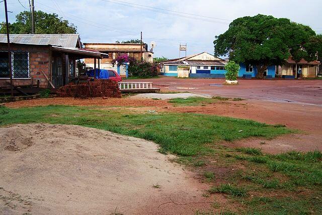 Rue en terre battue avec bâtiments colorés et voiture rouge, village près de Lethem, Guyana