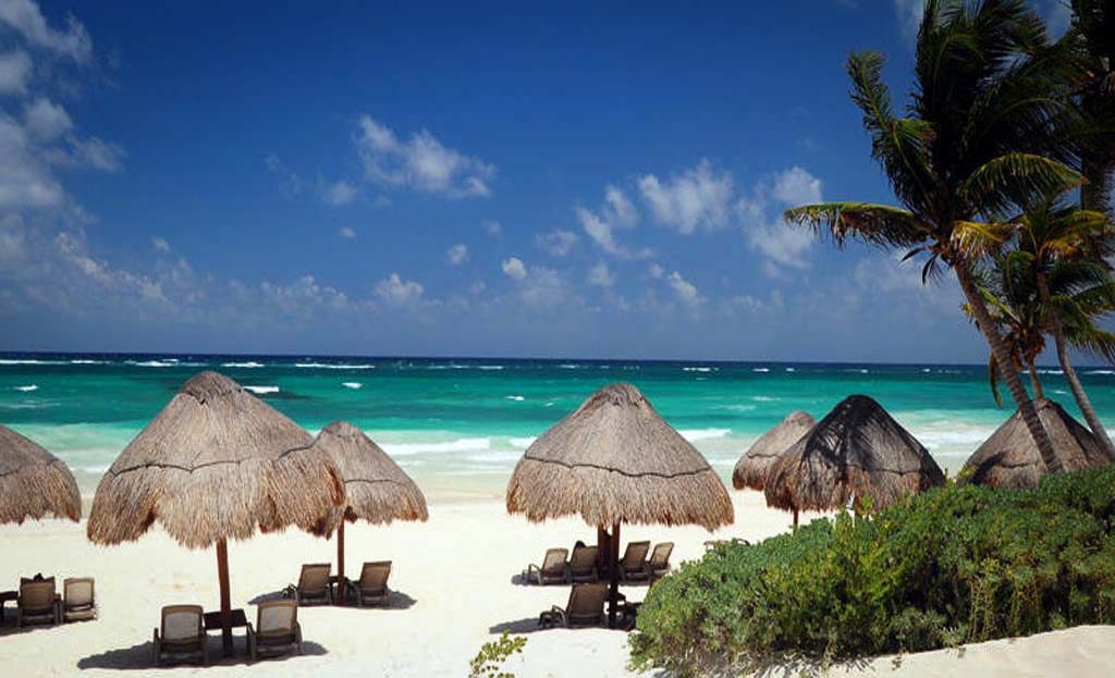 Plage de Tulum avec parasols en palapa, transats et palmiers face à la mer turquoise