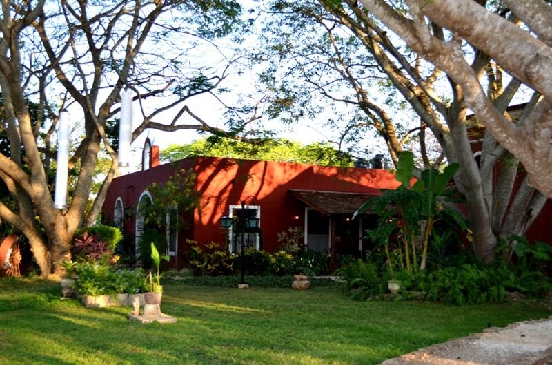 Bâtiment rouge de style hacienda entouré d'arbres et jardin verdoyant près de Merida, Mexique