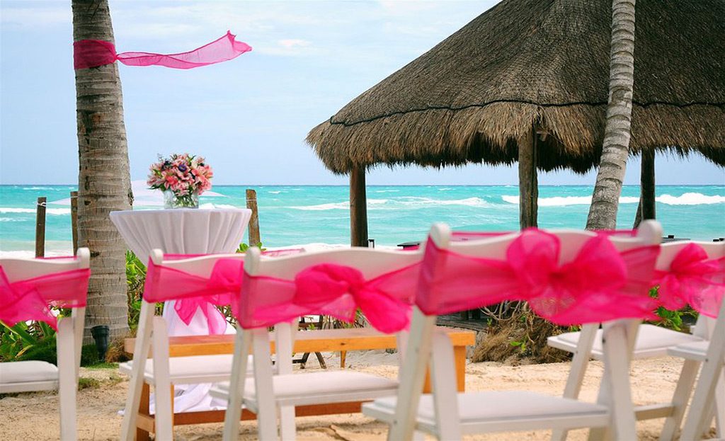 Chaises blanches nouées de rubans roses préparées pour une cérémonie sur la plage à Tulum, Mexique