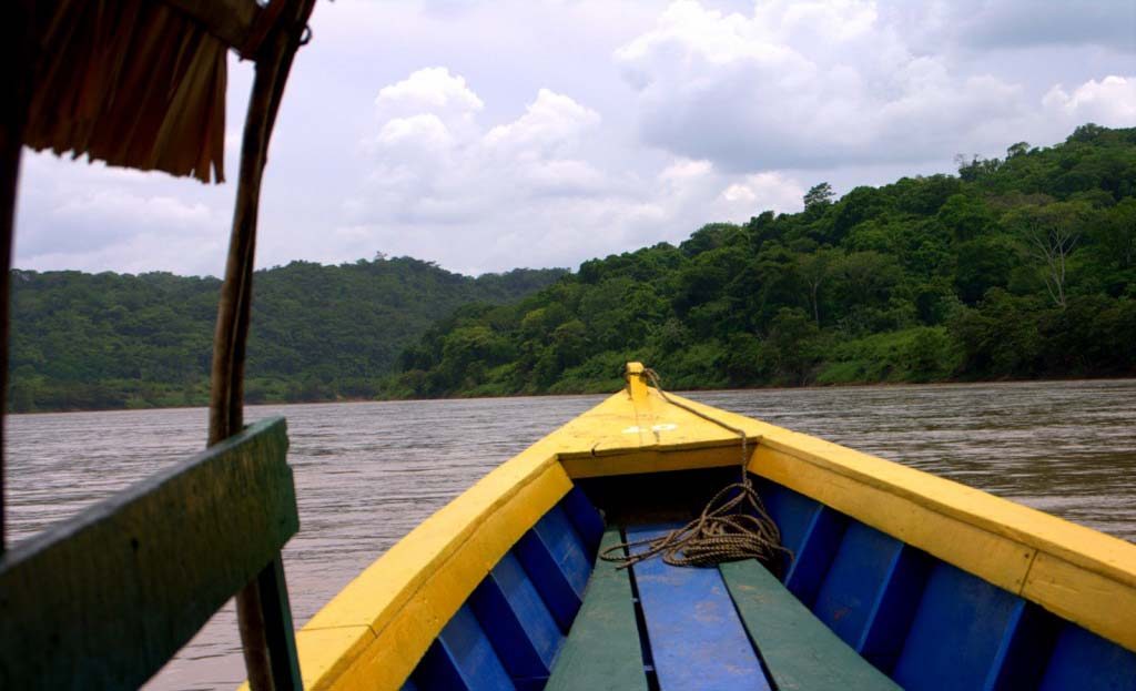 Bateau traditionnel jaune et bleu naviguant sur la rivière Usumacinta bordée de jungle, Chiapas