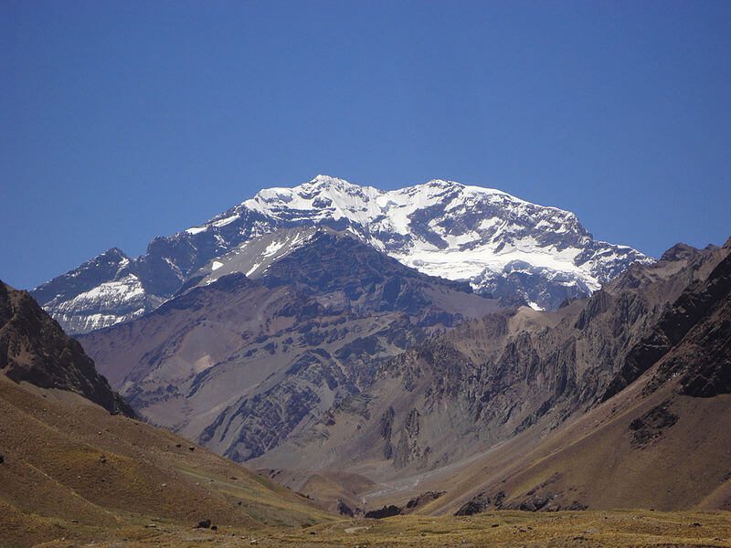 Sommet enneigé de la cordillère des Andes dominant une vallée aride et rocailleuse