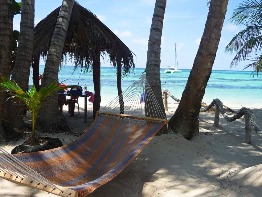 Hamac à rayures entre cocotiers sur plage caribéenne, catamaran ancré au large au Nicaragua