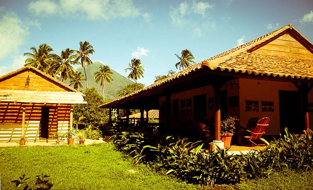 Maisons en bois à toits de tuiles avec palmiers et un volcan en arrière-plan, île d'Ometepe, Nicaragua