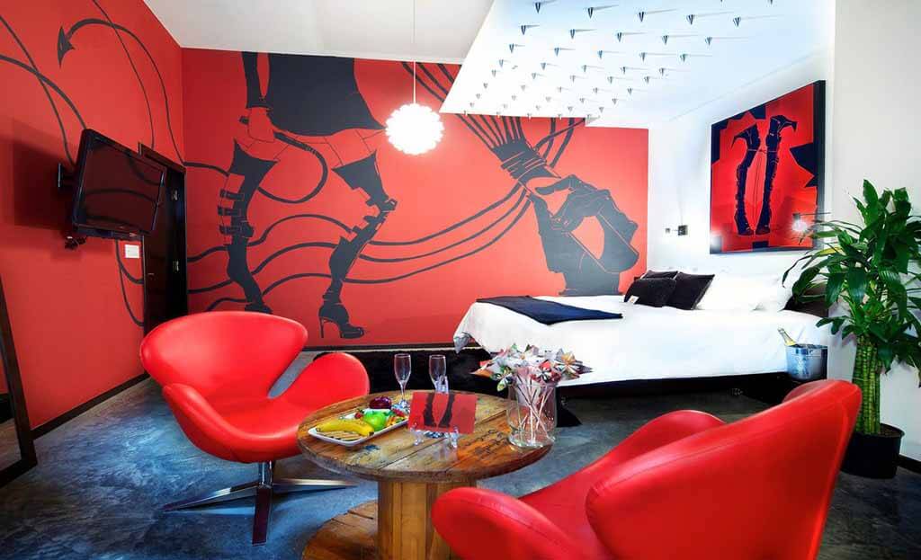 Chambre d'hôtel design avec fauteuils rouges, lit blanc et fresque murale artistique noire et rouge