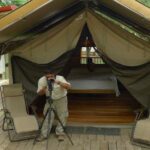 Homme photographiant devant une tente-bungalow avec lit et chaises, camp du Darien au Panama