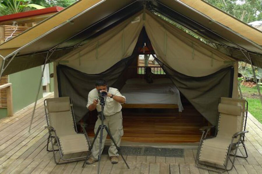 Homme photographiant devant une tente-bungalow avec lit et chaises, camp du Darien au Panama