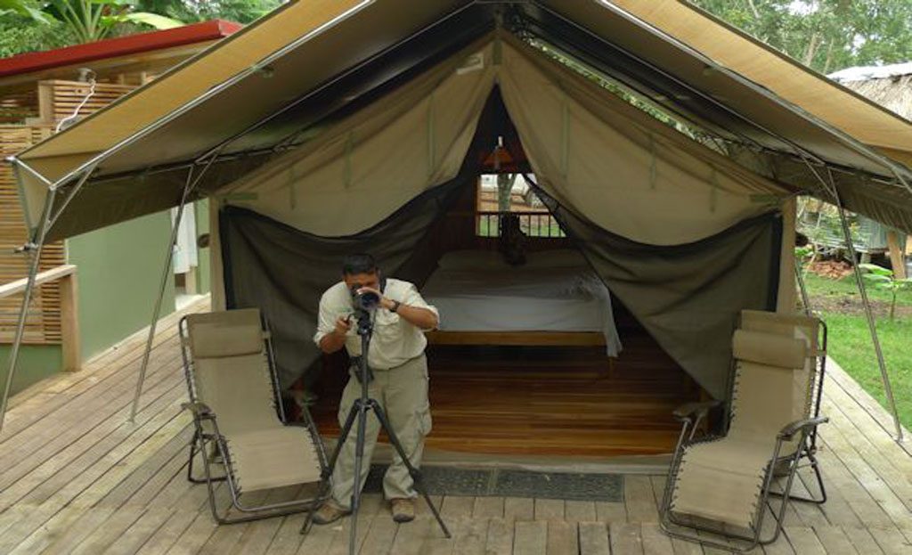 Homme photographiant devant une tente-bungalow avec lit et chaises, camp du Darien au Panama
