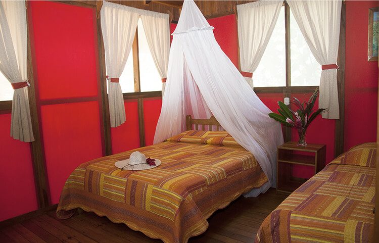 Chambre aux murs rouges avec lit à moustiquaire blanche, chapeau de paille et fleurs tropicales, Costa Rica