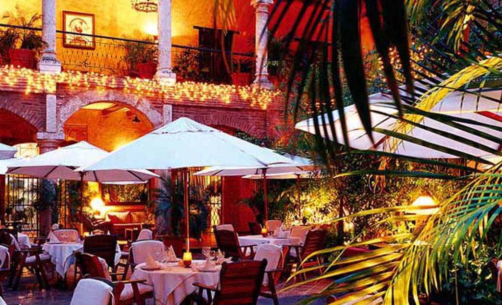 Terrasse de restaurant illuminée avec parasols et tables dressées dans un patio colonial à Saint-Domingue