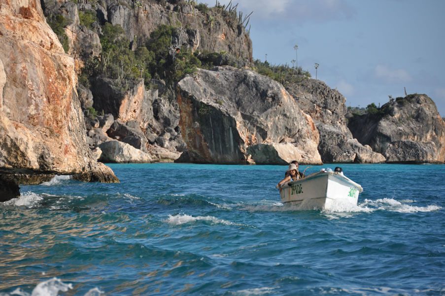 Petit bateau naviguant près de falaises rocheuses en bord de mer turquoise, République Dominicaine