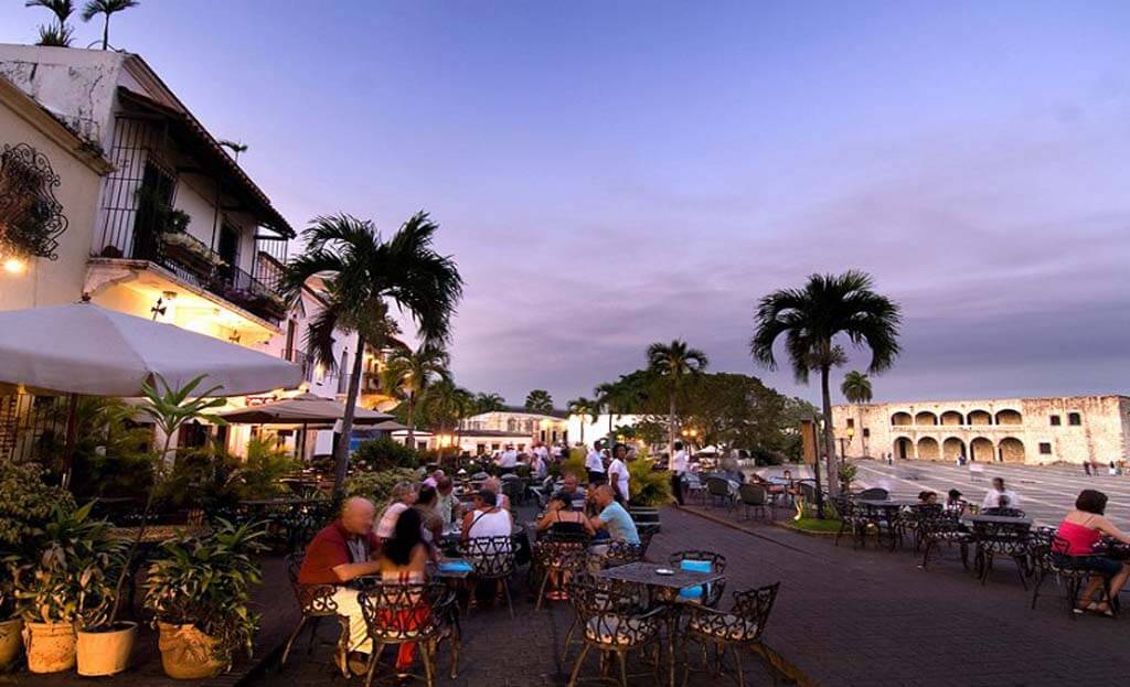 Terrasse de café avec palmiers au crépuscule, touristes attablés dans la vieille ville de Santo Domingo