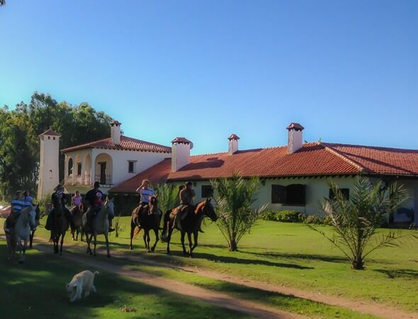 Groupe de cavaliers à cheval devant une estancia à toit de tuiles en Uruguay