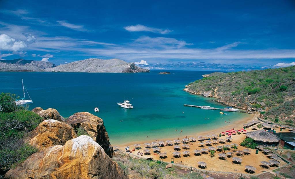 Vue aérienne d'une baie avec plage, parasols en paille, bateaux et montagnes rocheuses, parc national de Mochima, Venezuela