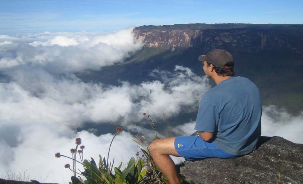 Homme assis au bord du mont Roraima, contemplant les nuages et falaises, Venezuela