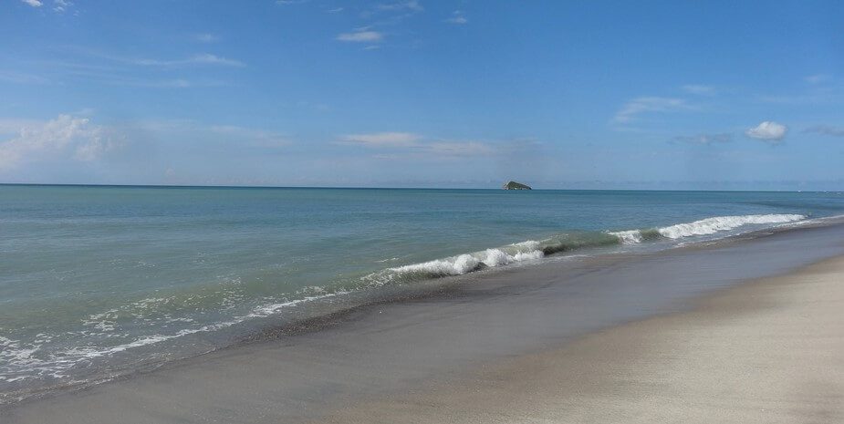 Plage de sable gris avec vagues et petit îlot au large, Santa Clara, Panama