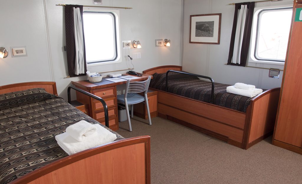 Cabine double avec deux lits, bureau et hublots à bord du navire d'expédition en Antarctique