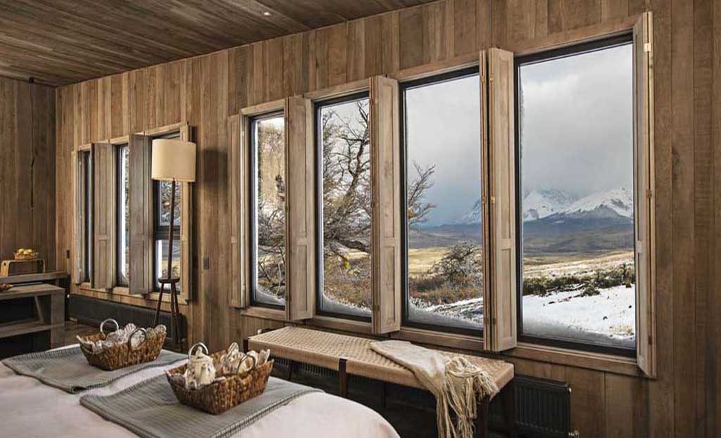 Chambre en bois avec grandes fenêtres donnant sur la steppe enneigée de Patagonie chilienne
