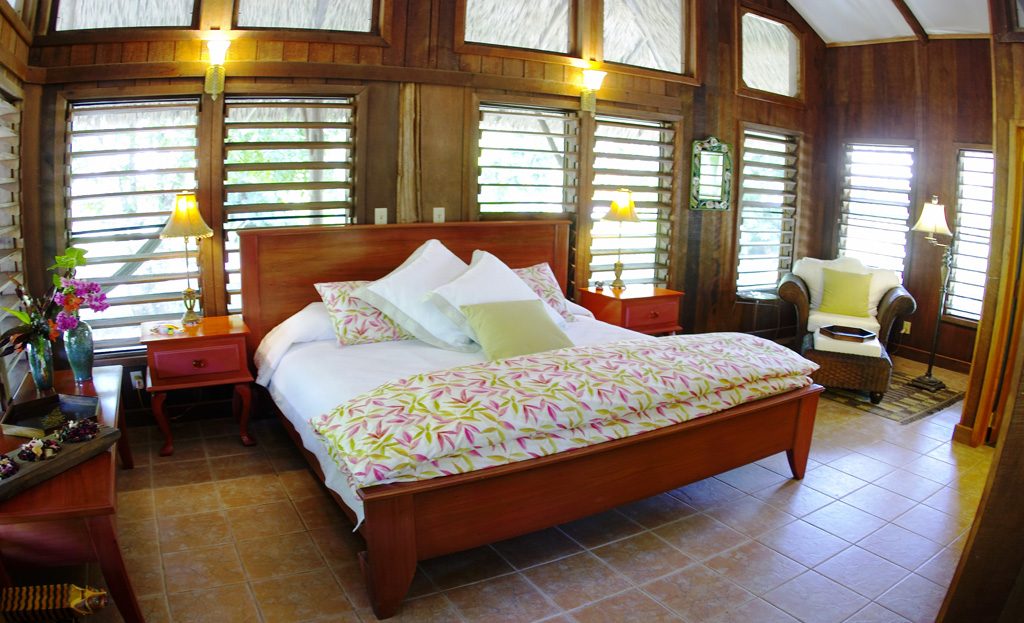 Chambre en bois avec grand lit, fauteuil en osier et volets persiennes dans un lodge du Belize