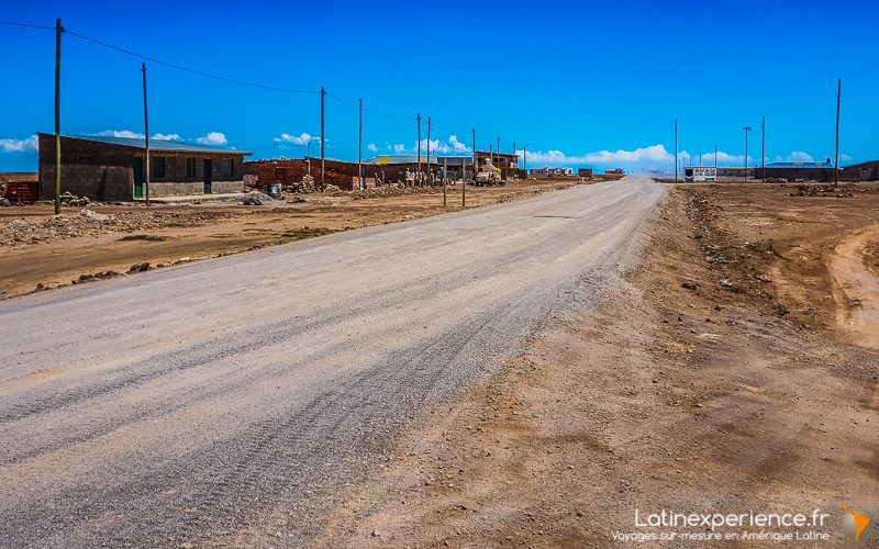 Route en terre traversant un village de l'Altiplano bolivien en plein jour, ciel bleu