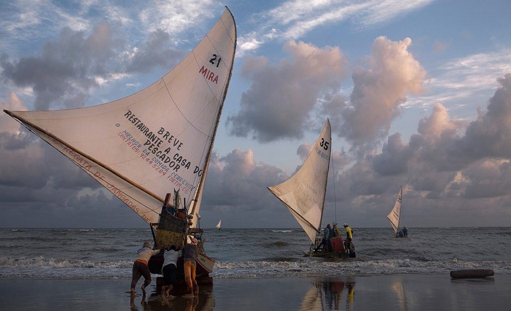 Pêcheurs poussant une jangada à voile depuis la plage de Pontal do Maceió, Brésil