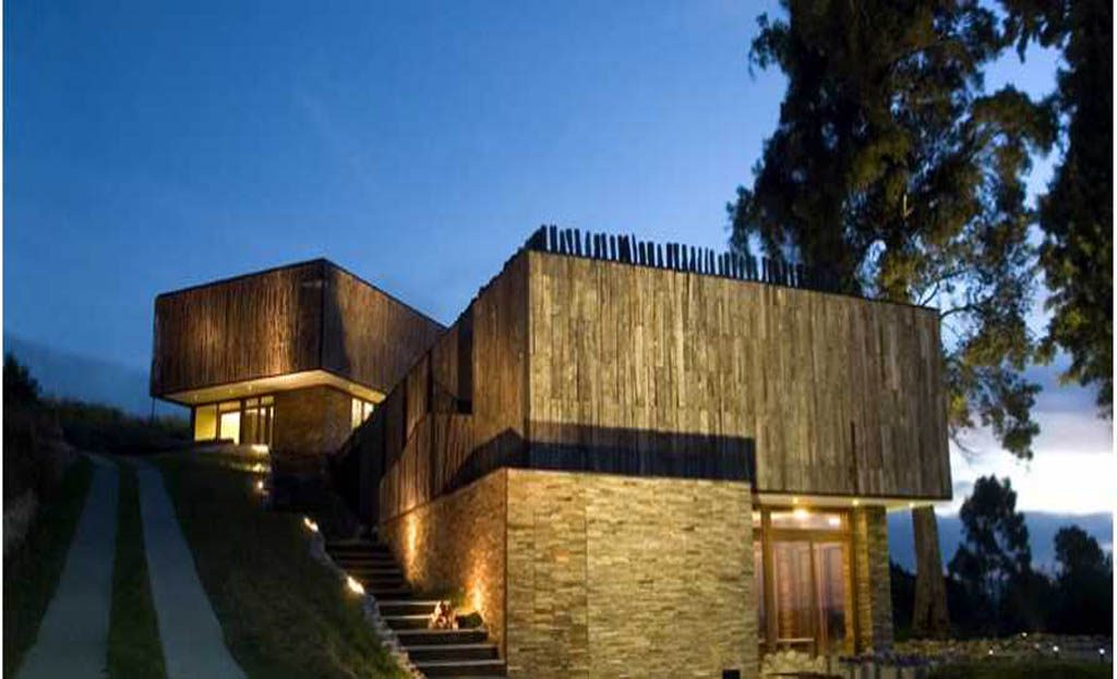 Maison moderne en bois et pierre éclairée au crépuscule, escalier extérieur, Chili