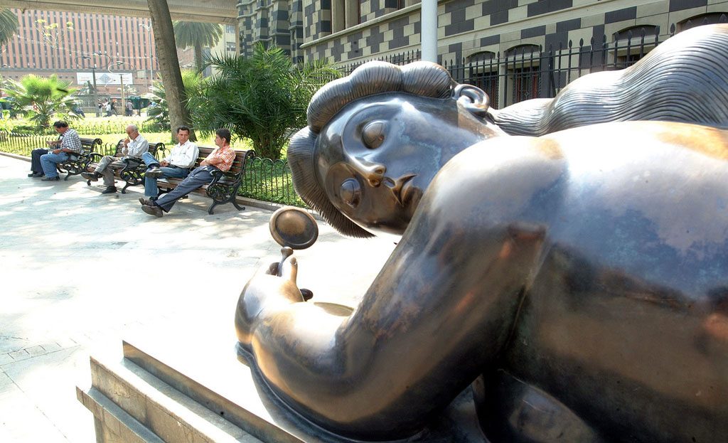 Sculpture en bronze de Botero sur une place à Medellín, avec des passants assis sur des bancs
