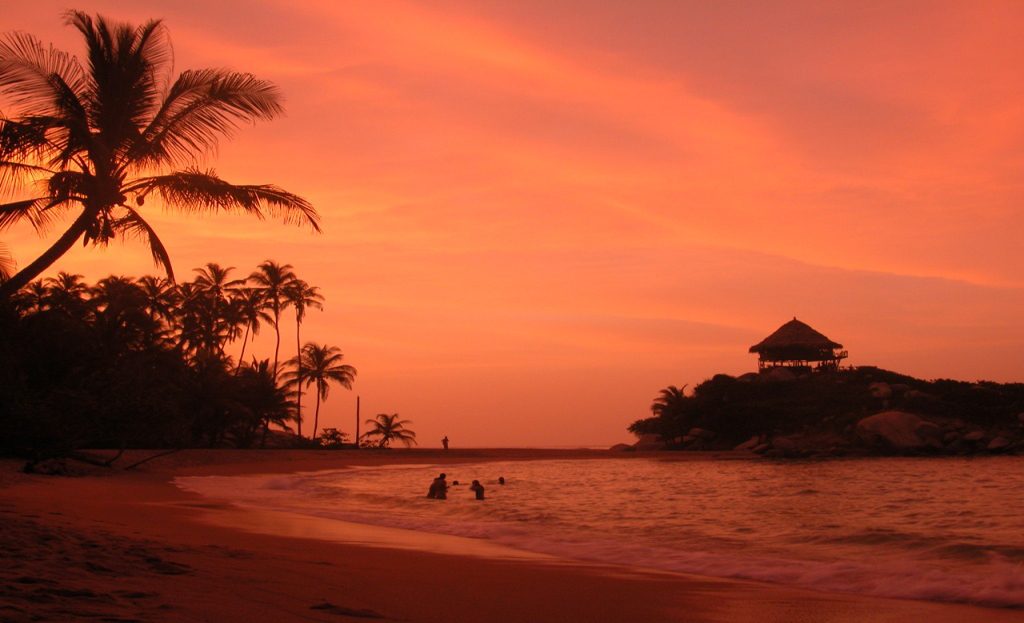 Coucher de soleil orange sur une plage de palmiers avec baigneurs près de Santa Marta, Colombie