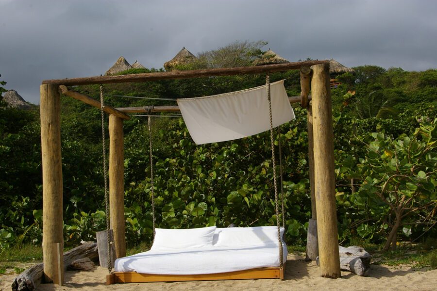 Lit balancelle en bois avec voile blanc sur plage de sable, végétation tropicale, Santa Marta, Colombie