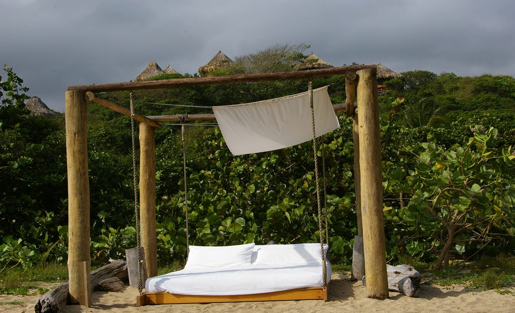 Lit balancelle en bois avec voile blanc sur plage de sable, végétation tropicale, Santa Marta, Colombie