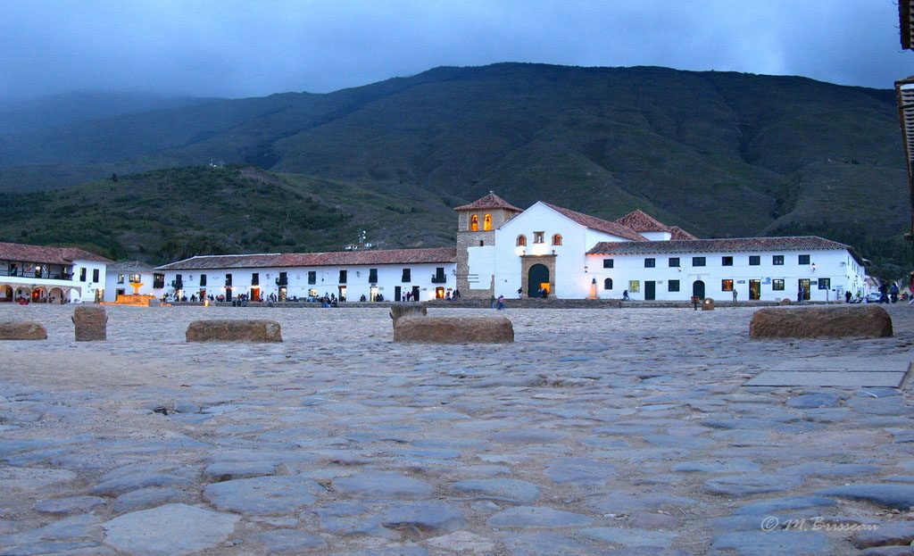 Place pavée de Villa de Leyva au crépuscule, église illuminée et montagnes en arrière-plan