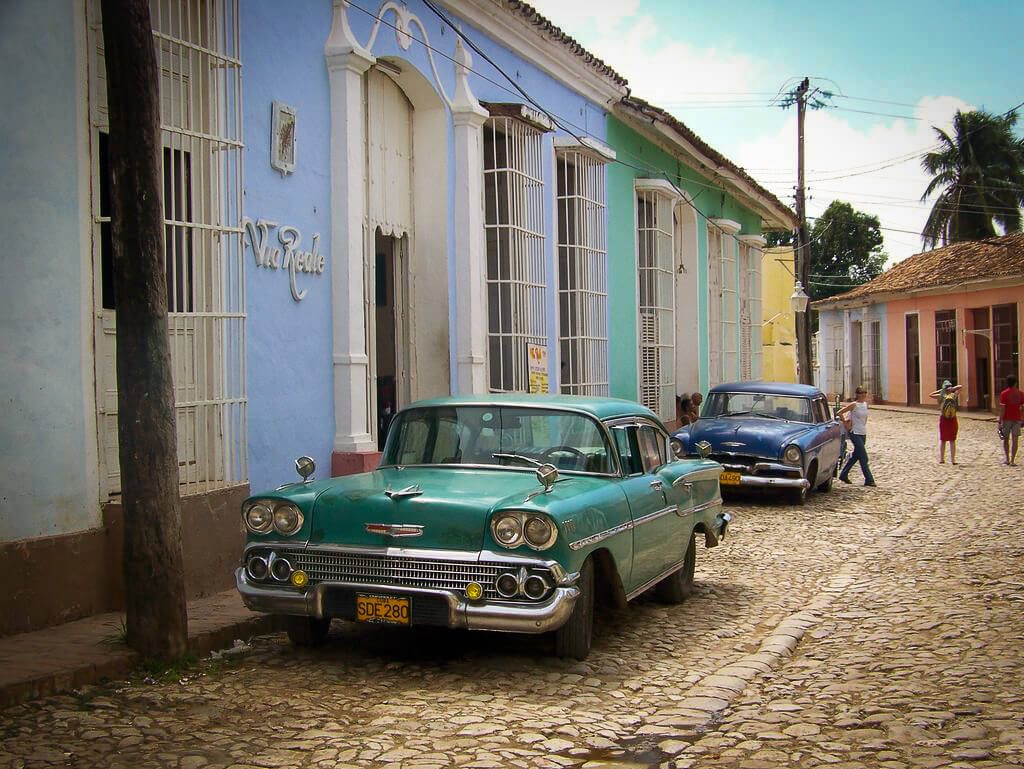 Voitures américaines anciennes garées devant des façades colorées dans une rue pavée de Trinidad, Cuba