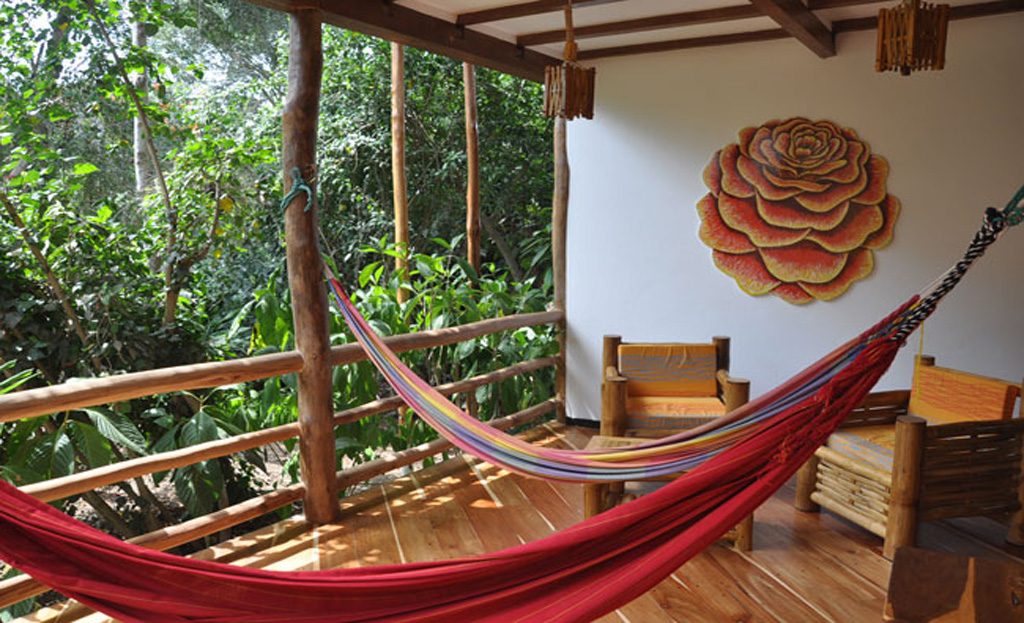 Terrasse en bois avec hamac coloré et fauteuils, entourée de végétation tropicale près de Puerto López