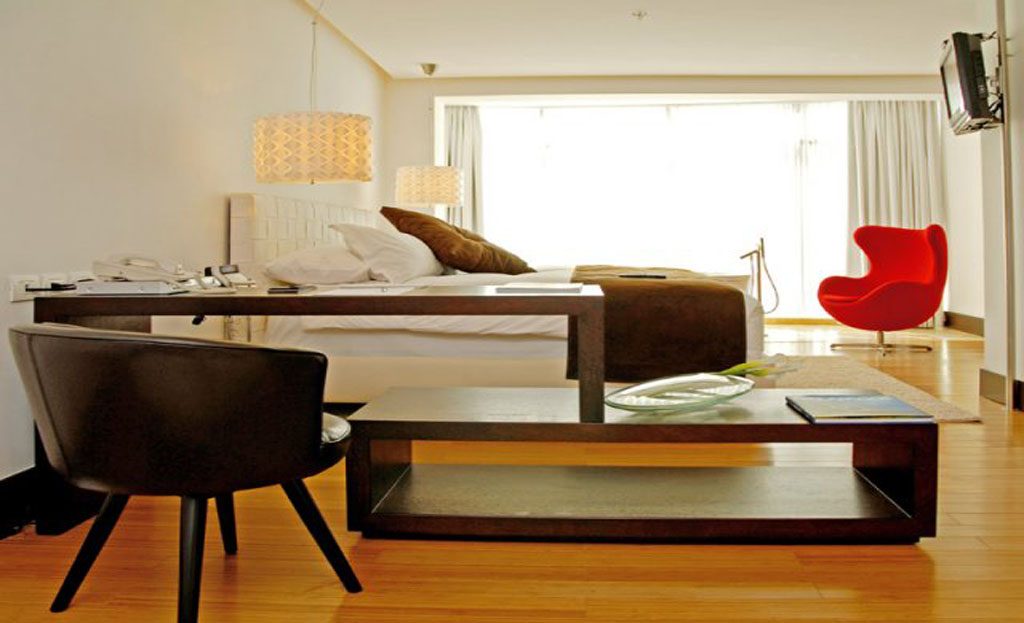 Chambre d'hôtel moderne à Quito avec lit, bureau, fauteuil rouge et parquet en bois