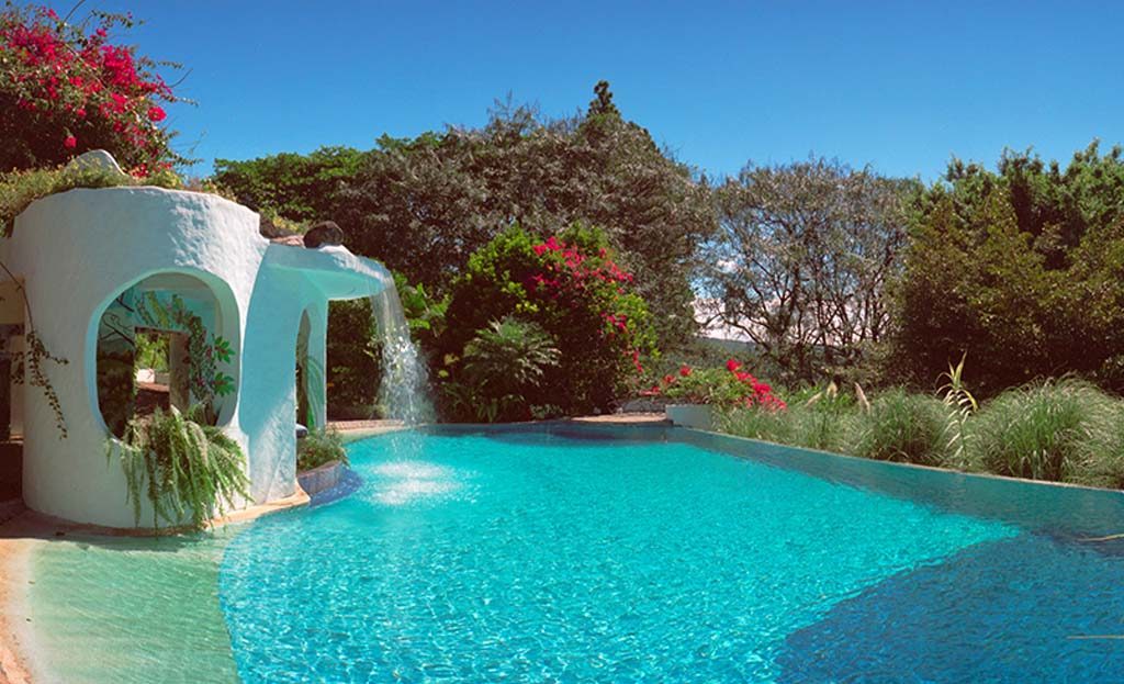 Piscine turquoise avec cascade et structure blanche sculptée, entourée de bougainvilliers dans un jardin tropical du Costa Rica