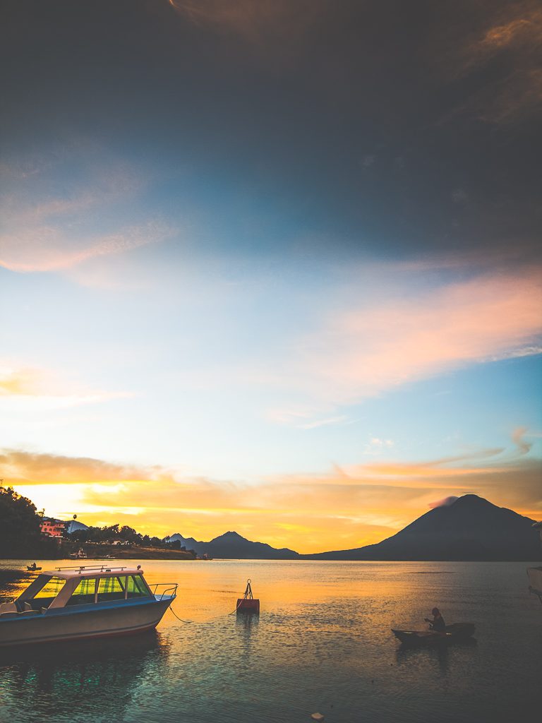 Coucher de soleil sur le lac Atitlan avec bateaux amarrés et volcans en silhouette, Guatemala