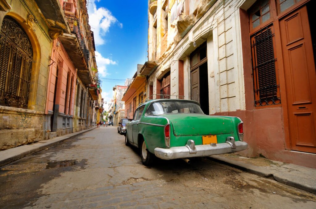 Voiture ancienne verte garée dans une ruelle pavée aux façades délabrées de La Havane, Cuba
