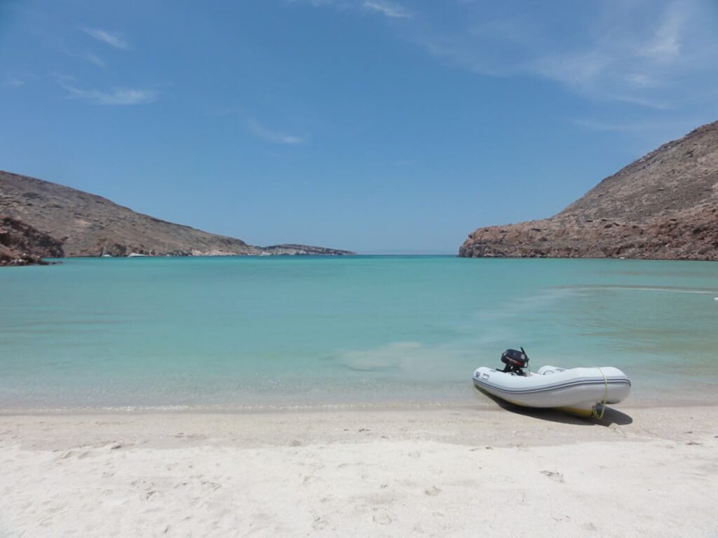 Plage de sable blanc avec canot pneumatique échoué, eaux turquoise et collines désertiques près de La Paz