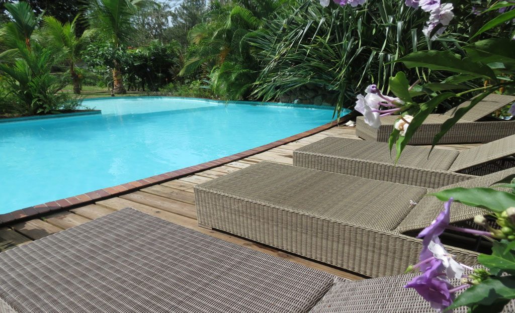 Piscine turquoise entourée de palmiers avec transats en rotin sur terrasse en bois, Panama