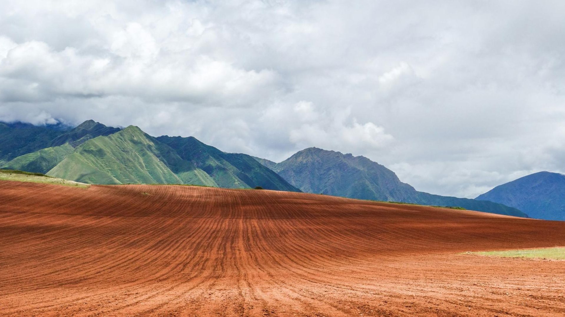 Champ de terre rouge labouré avec montagnes verdoyantes de la vallée sacrée au Pérou